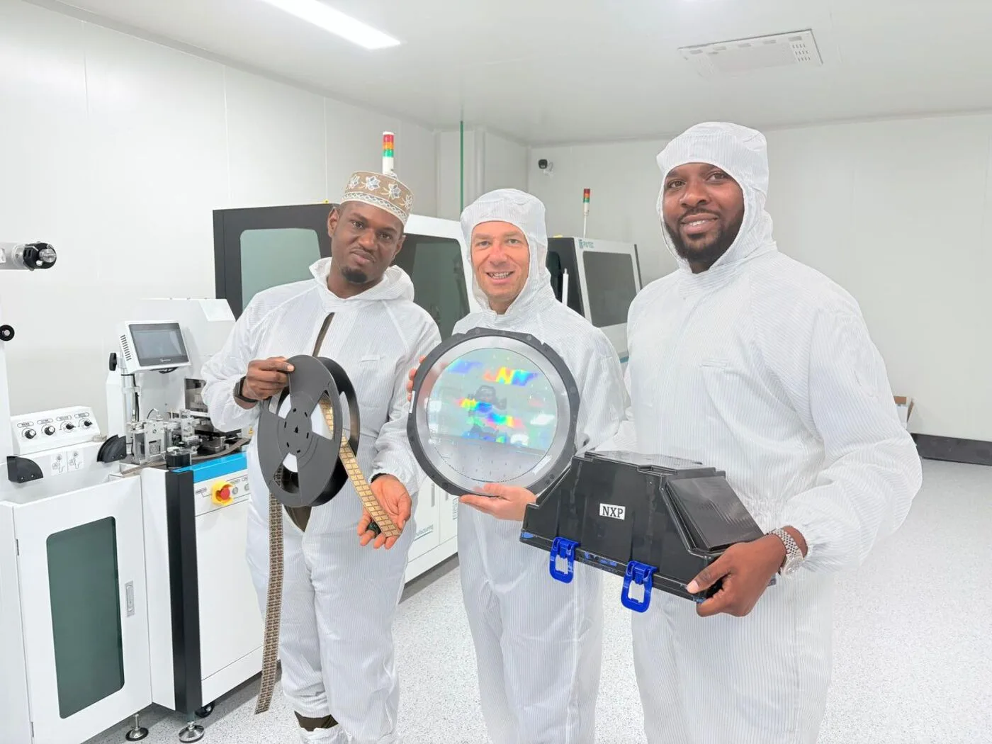 ASMC engineers holding a wafer, component reel and packaging in the cleanroom